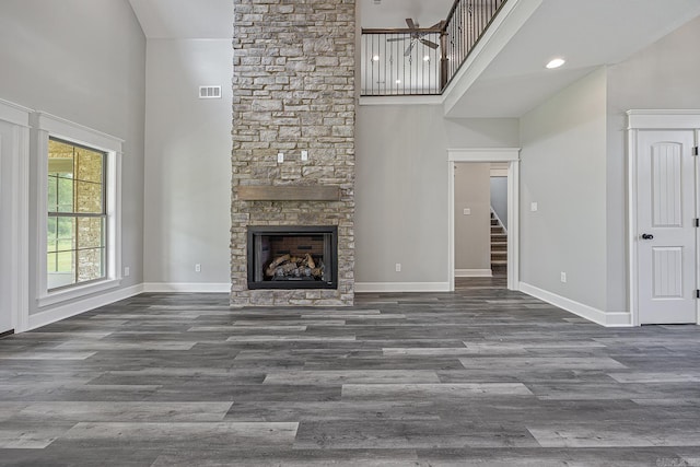 unfurnished living room featuring a stone fireplace, dark wood-type flooring, and a high ceiling