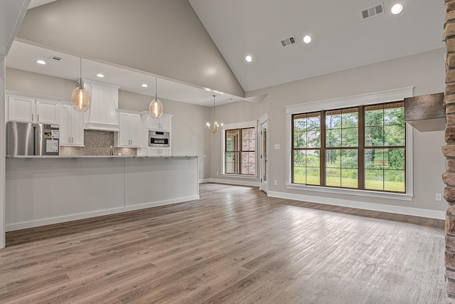 unfurnished living room with hardwood / wood-style floors, an inviting chandelier, high vaulted ceiling, and sink