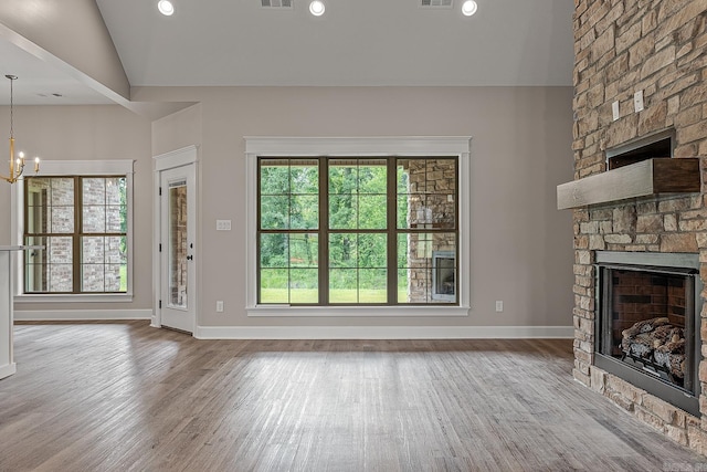 unfurnished living room featuring a stone fireplace, light hardwood / wood-style flooring, lofted ceiling, and a notable chandelier