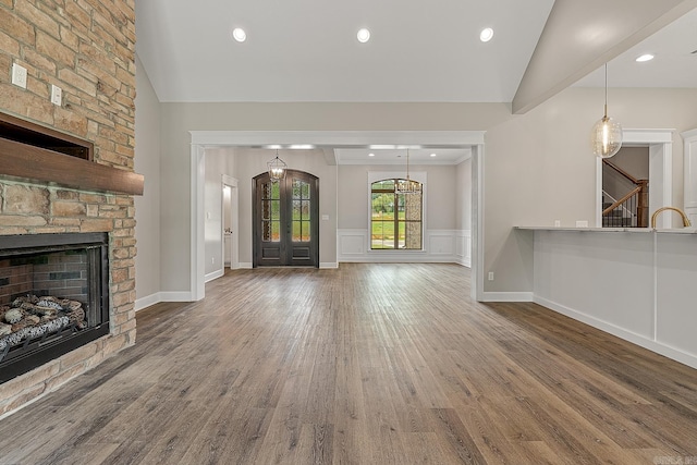 unfurnished living room featuring french doors, sink, hardwood / wood-style floors, a stone fireplace, and lofted ceiling