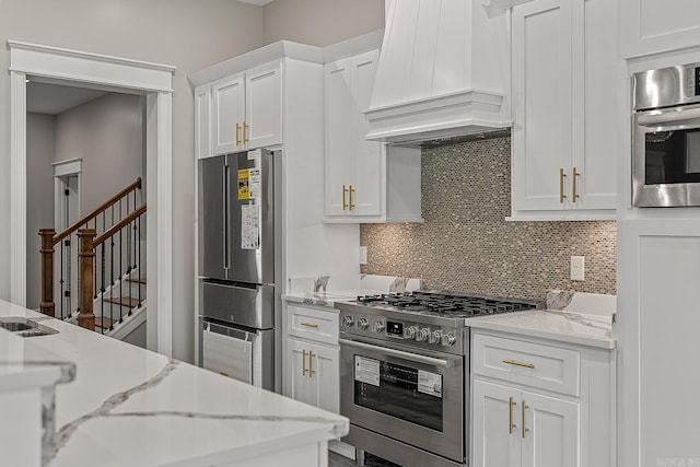 kitchen featuring tasteful backsplash, white cabinetry, premium range hood, and stainless steel appliances