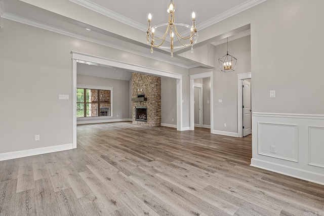 unfurnished living room featuring hardwood / wood-style floors, a notable chandelier, a stone fireplace, and crown molding