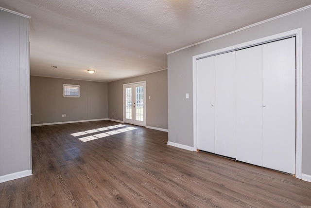 unfurnished bedroom with a textured ceiling, ornamental molding, dark wood-type flooring, and french doors