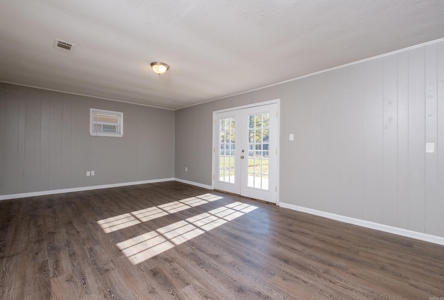 spare room featuring french doors, wooden walls, ornamental molding, and dark wood-type flooring