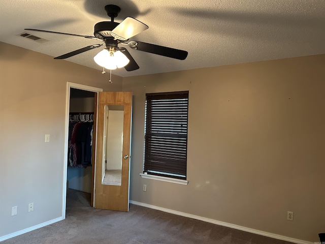 unfurnished bedroom with ceiling fan, a closet, a textured ceiling, and dark colored carpet