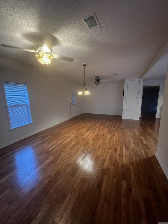 empty room with dark hardwood / wood-style flooring, ceiling fan with notable chandelier, and a textured ceiling