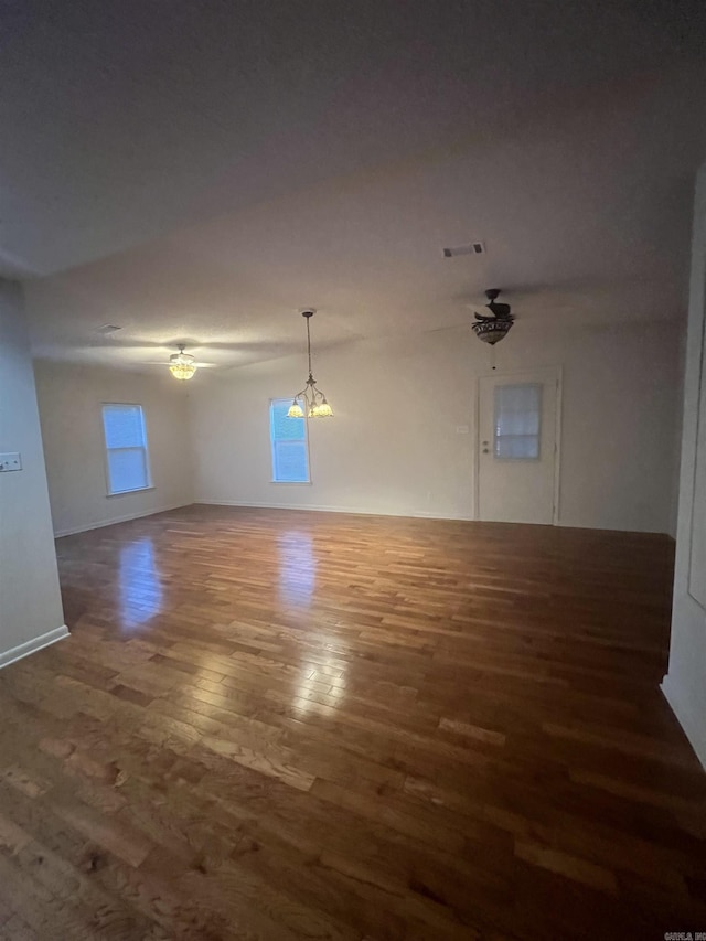 spare room with ceiling fan with notable chandelier and dark hardwood / wood-style floors