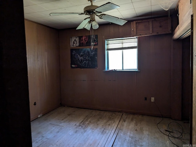 empty room with ceiling fan, light hardwood / wood-style floors, and wooden walls