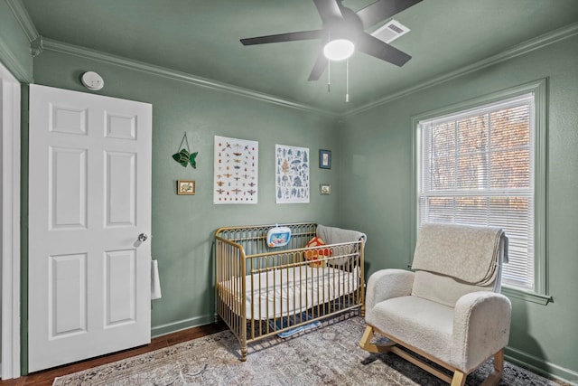 bedroom with hardwood / wood-style flooring, ceiling fan, a crib, and crown molding