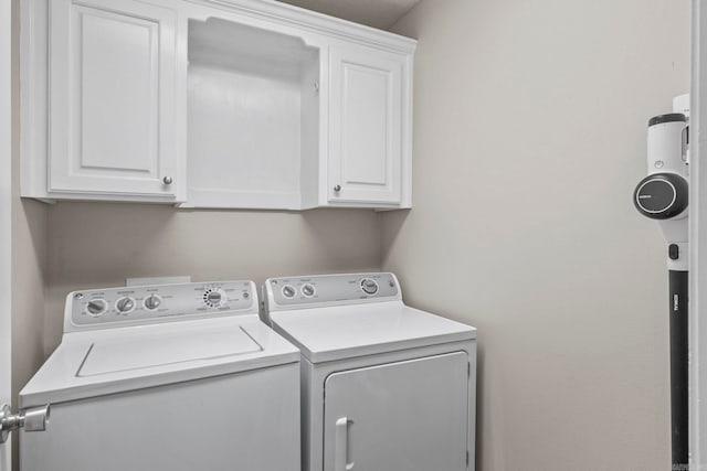 clothes washing area with separate washer and dryer and cabinets