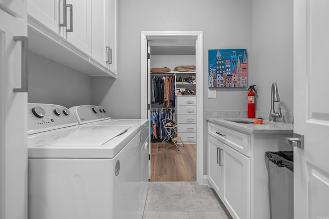 laundry area featuring washing machine and clothes dryer, sink, cabinets, and light hardwood / wood-style floors