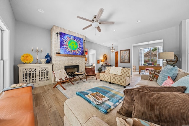 living room with a brick fireplace, ceiling fan, and light wood-type flooring