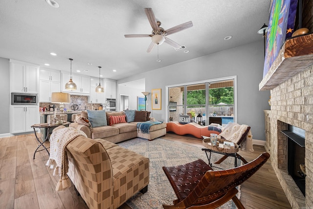 living room with ceiling fan, light hardwood / wood-style floors, a textured ceiling, and a brick fireplace