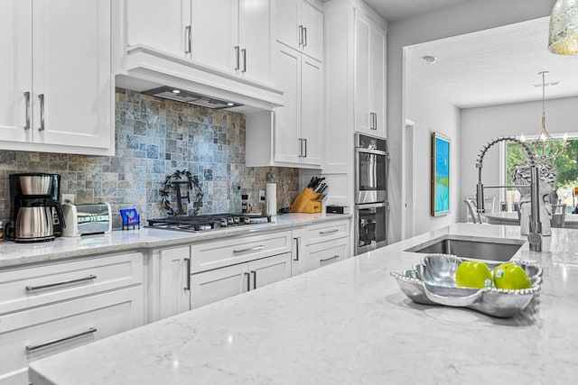 kitchen with pendant lighting, premium range hood, white cabinetry, and sink