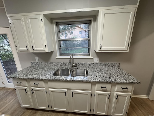 kitchen featuring white cabinets, light wood-type flooring, light stone countertops, and sink