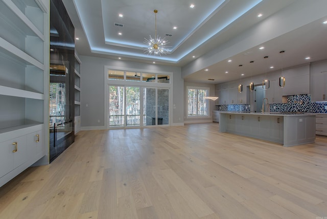 unfurnished living room with a tray ceiling, sink, light hardwood / wood-style floors, and a notable chandelier