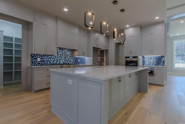 kitchen with a large island with sink, light stone countertops, oven, and light wood-type flooring