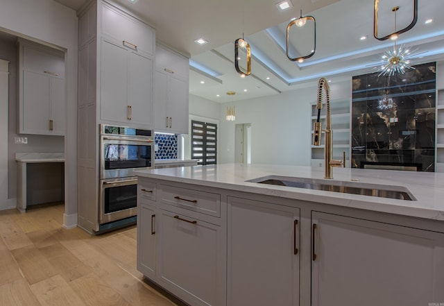 kitchen featuring double oven, light stone counters, sink, and light hardwood / wood-style floors