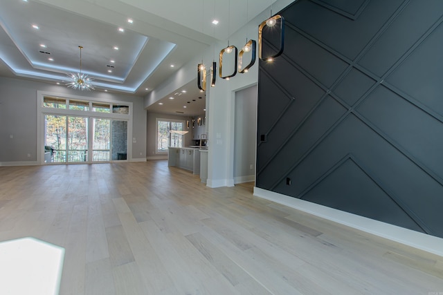 unfurnished living room with a chandelier, a tray ceiling, and light hardwood / wood-style floors