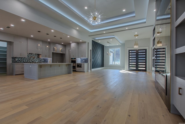 kitchen with pendant lighting, backsplash, a spacious island, a tray ceiling, and light hardwood / wood-style floors