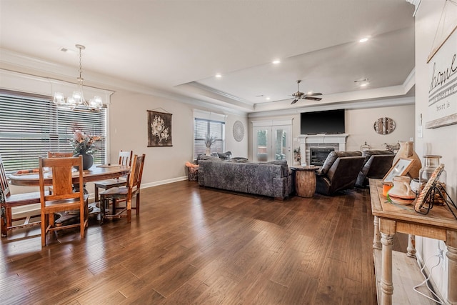 living room featuring ceiling fan with notable chandelier, dark hardwood / wood-style floors, a tray ceiling, and ornamental molding