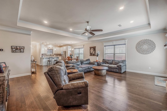 living room featuring a tray ceiling, crown molding, and dark wood-type flooring