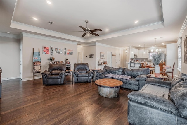 living room featuring ceiling fan, ornamental molding, dark wood-type flooring, and a tray ceiling