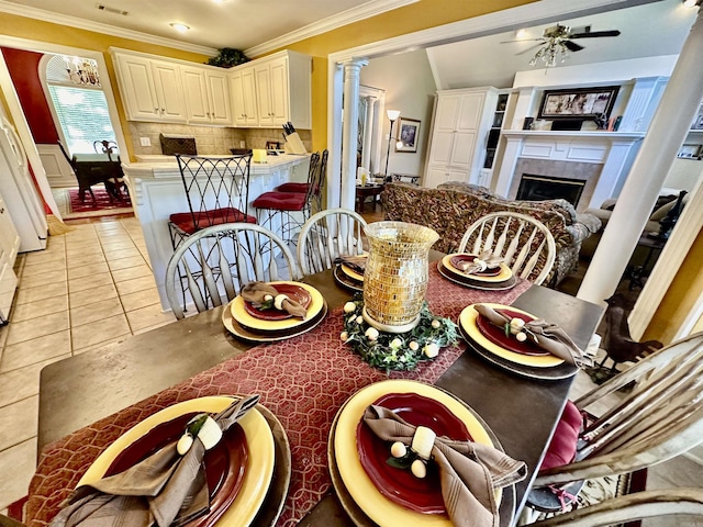 tiled dining area featuring a fireplace, ornate columns, ceiling fan, and crown molding