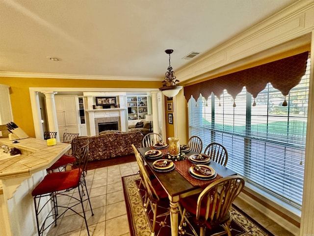 dining space with decorative columns, a tile fireplace, crown molding, and light tile patterned floors