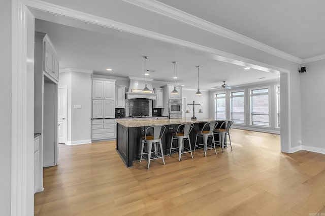 kitchen with pendant lighting, a spacious island, light hardwood / wood-style flooring, light stone counters, and a kitchen bar