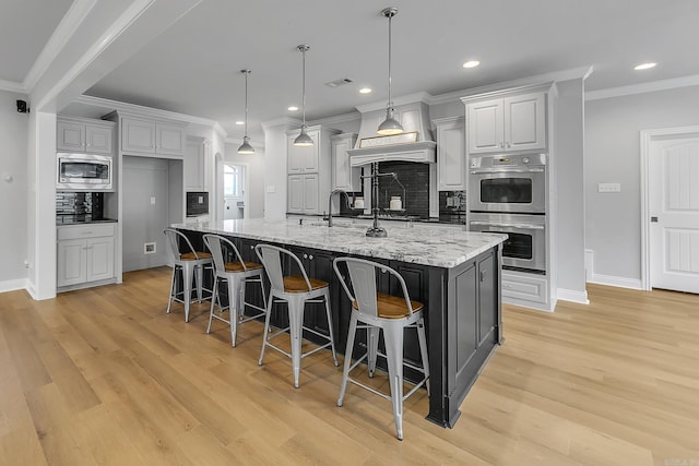 kitchen with light stone countertops, stainless steel appliances, light hardwood / wood-style flooring, decorative backsplash, and a center island with sink