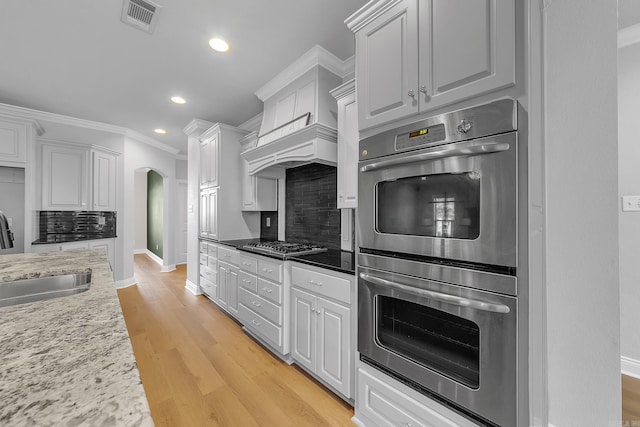 kitchen featuring sink, light hardwood / wood-style flooring, decorative backsplash, white cabinets, and appliances with stainless steel finishes