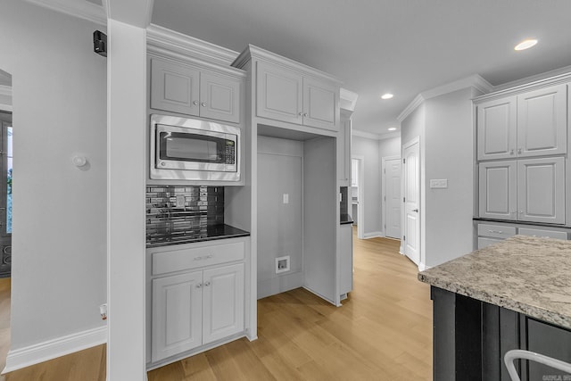 kitchen featuring stainless steel microwave, ornamental molding, backsplash, and light hardwood / wood-style flooring