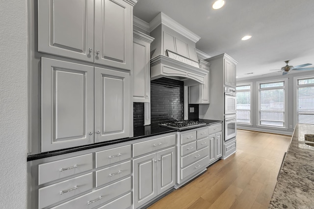 kitchen featuring decorative backsplash, ceiling fan, light wood-type flooring, light stone counters, and stainless steel appliances