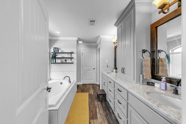 bathroom with hardwood / wood-style floors, vanity, ornamental molding, and tiled tub