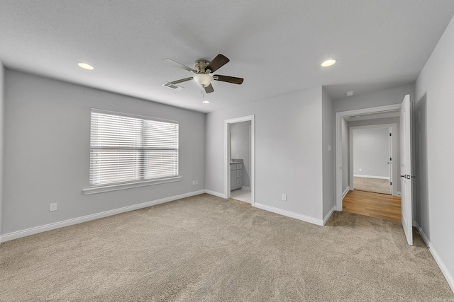 unfurnished bedroom with ceiling fan, ensuite bathroom, and light carpet