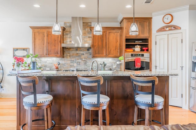 kitchen featuring stainless steel oven, light hardwood / wood-style flooring, light stone counters, and wall chimney range hood