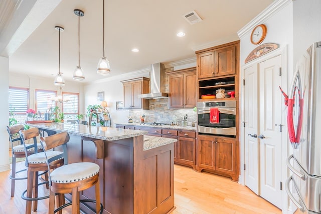 kitchen with wall chimney range hood, light stone counters, decorative light fixtures, a breakfast bar, and appliances with stainless steel finishes