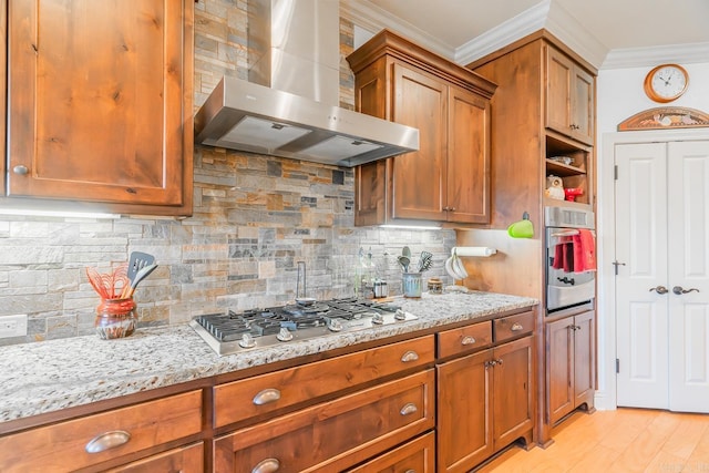 kitchen with backsplash, wall chimney range hood, light wood-type flooring, appliances with stainless steel finishes, and light stone counters