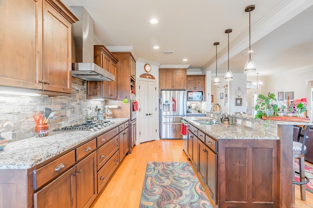 kitchen with sink, stainless steel appliances, wall chimney range hood, pendant lighting, and a kitchen bar