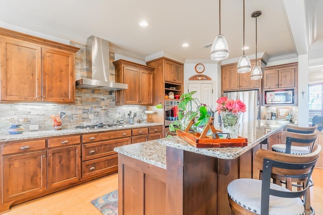 kitchen with a center island, a kitchen breakfast bar, hanging light fixtures, wall chimney exhaust hood, and appliances with stainless steel finishes