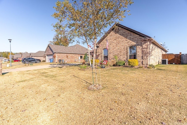 rear view of property featuring central AC unit, a garage, and a lawn