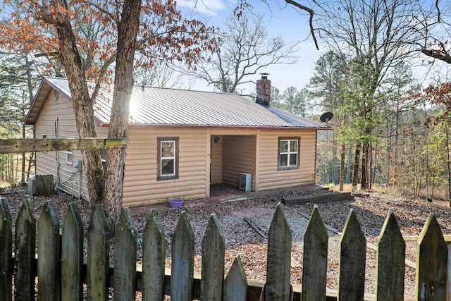 rustic home with metal roof, faux log siding, a chimney, and fence