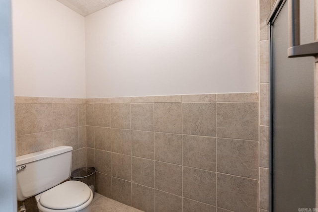 bathroom with a textured ceiling, an enclosed shower, tile walls, and toilet