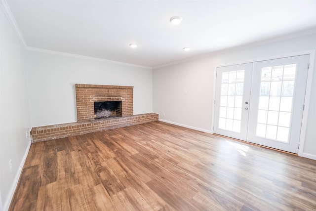 unfurnished living room featuring french doors, hardwood / wood-style flooring, a brick fireplace, and crown molding