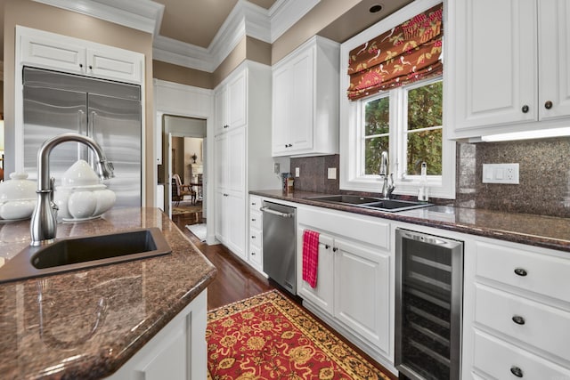 kitchen with white cabinetry, sink, beverage cooler, built in refrigerator, and dark stone counters