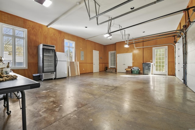 garage with electric panel, white fridge, a garage door opener, and wood walls