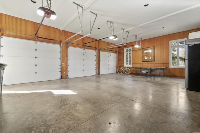 garage featuring wood walls, a garage door opener, and stainless steel refrigerator