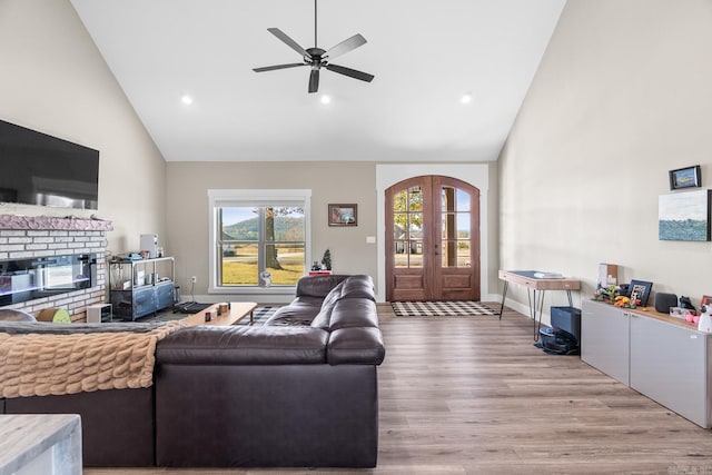 living room with ceiling fan, light wood-type flooring, high vaulted ceiling, and french doors