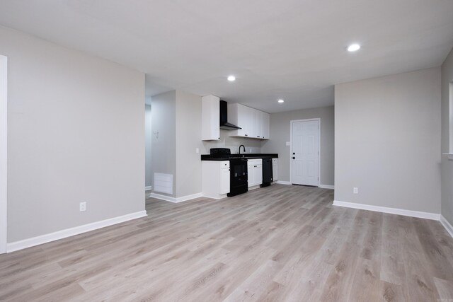 kitchen with white cabinets, wall chimney exhaust hood, black appliances, and light hardwood / wood-style floors